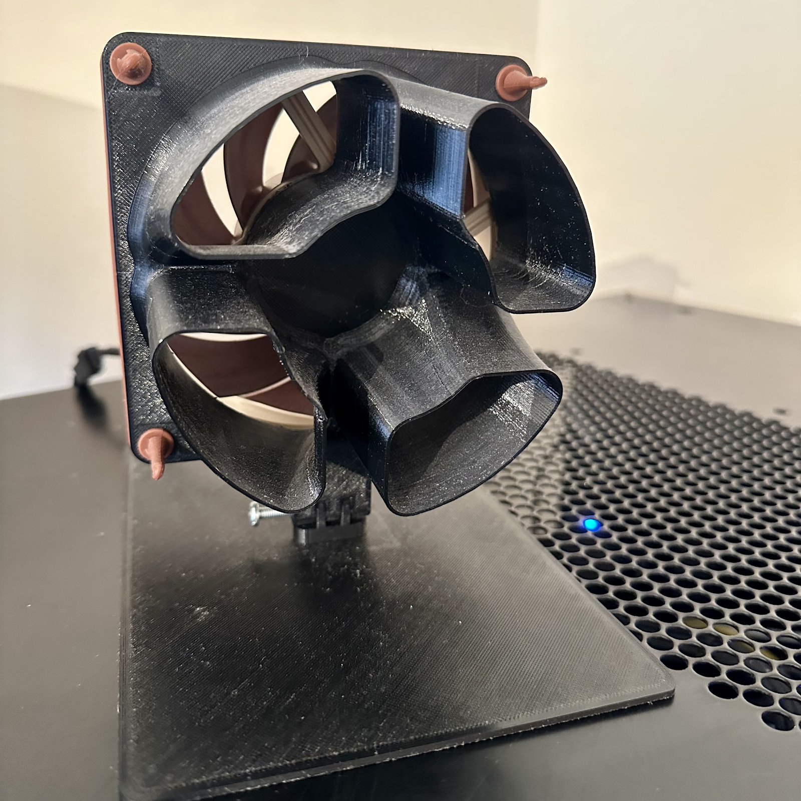 Brown Noctua 120mm fan held in a black 3D-printed laminar-flow housing and stand on top of a computer.
